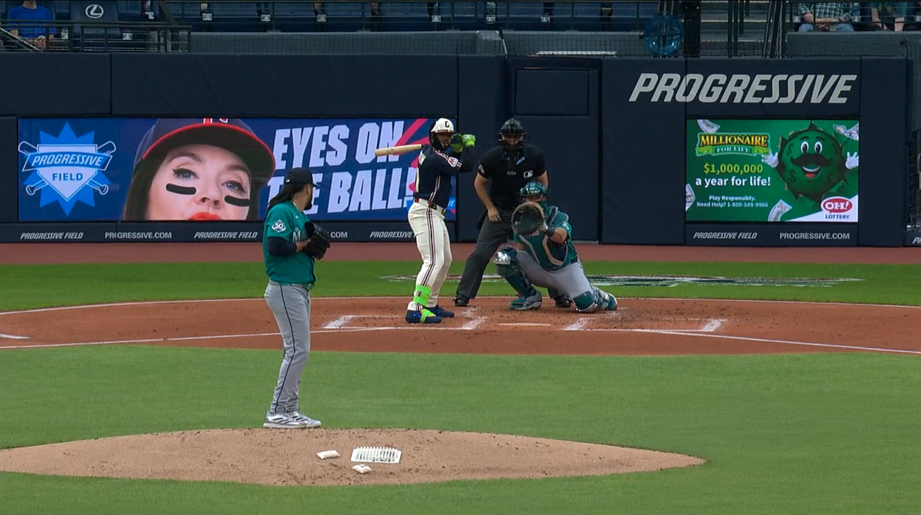 Behind-home-plate signage at Progressive Field during a game, showing a Millionaire For Life board with the green money-ball character and the $1,000,000 a year for life message.