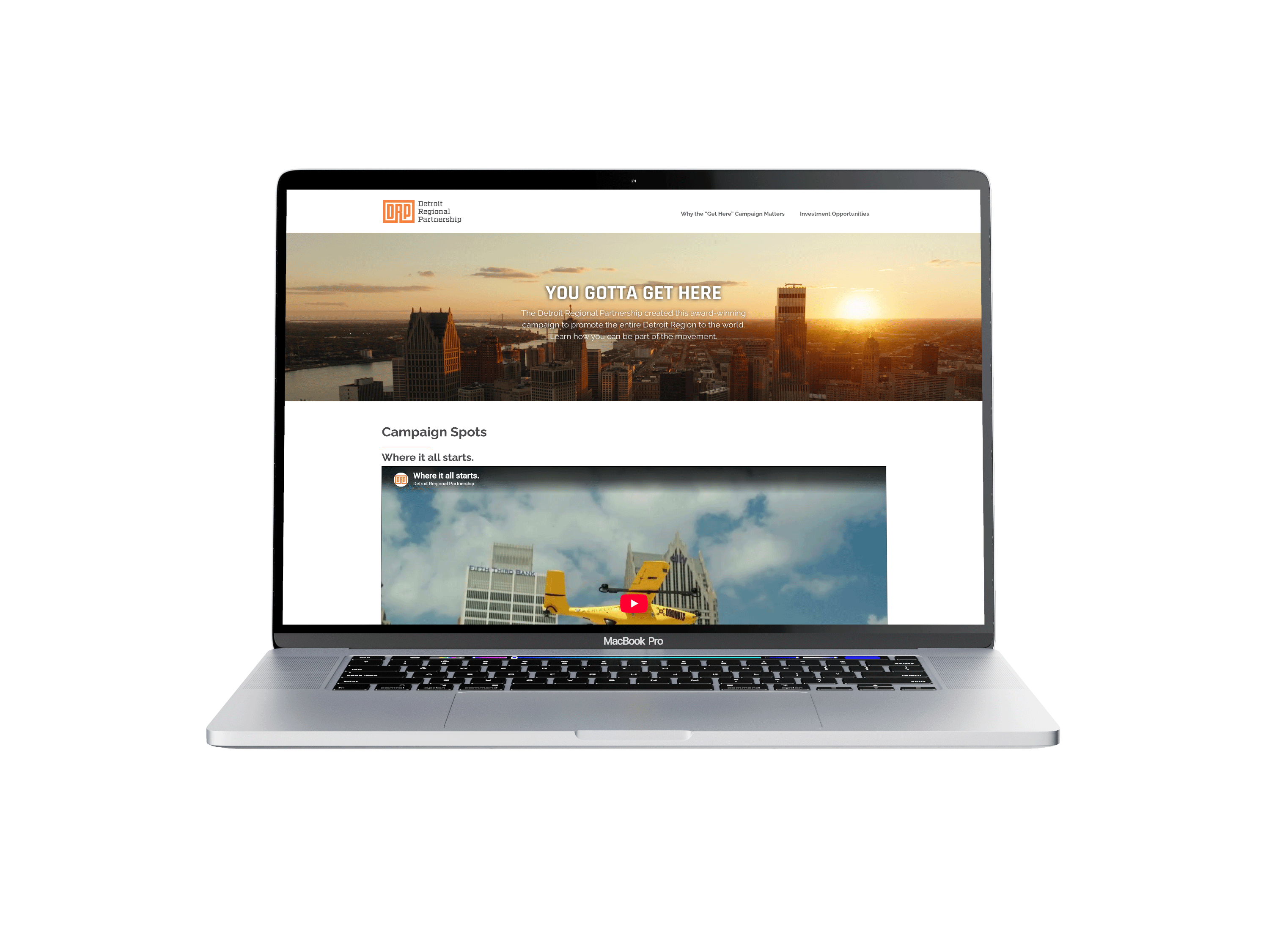 MacBook Pro showing the Get Here campaign landing page: a Detroit skyline at sunset with the headline You Gotta Get Here, above a Campaign Spots section.